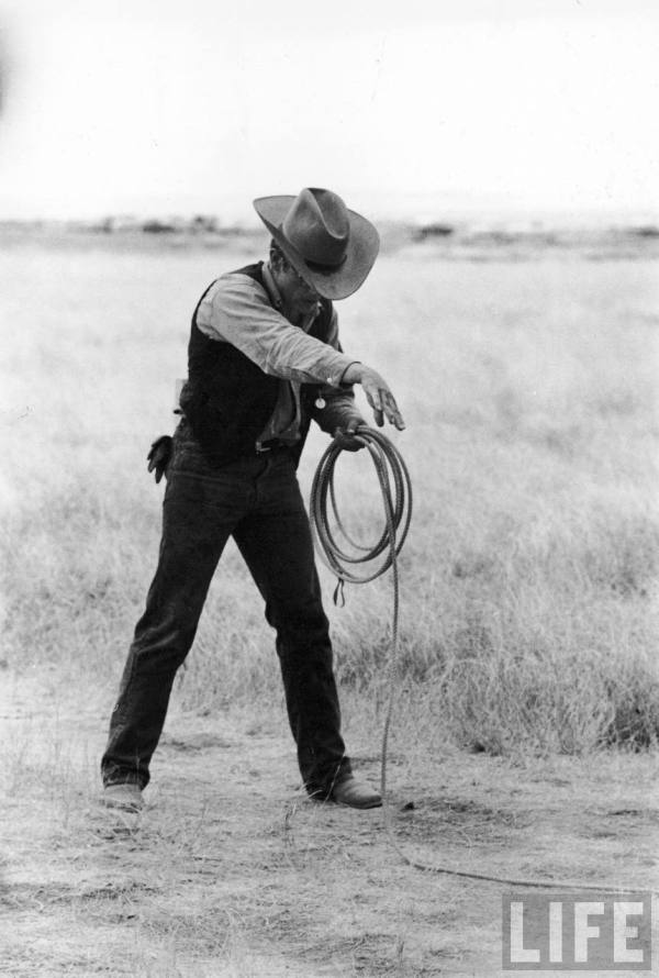 Actor James Dean clad in Western garb for his role, holding a coiled rope, on location for the movie "Giant."